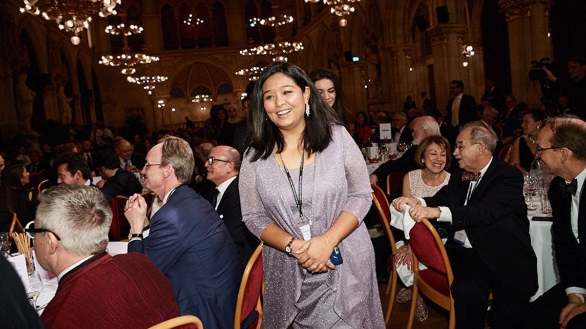 Kanika Ghocha walking to the stage in a ballroom filled with business and academic leaders.