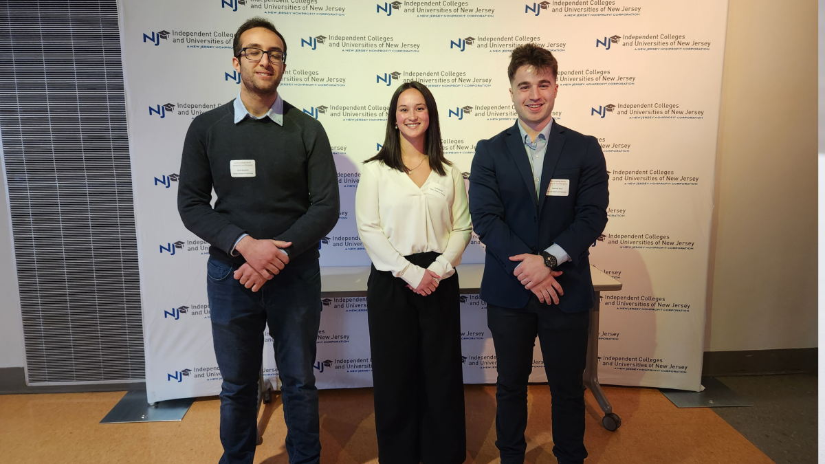 Amir Ibrahim ’25, Jenna Booth ’23 and Gabriel Sorci ’25 pose in front of a branded backdrop at ICUNJ 2023