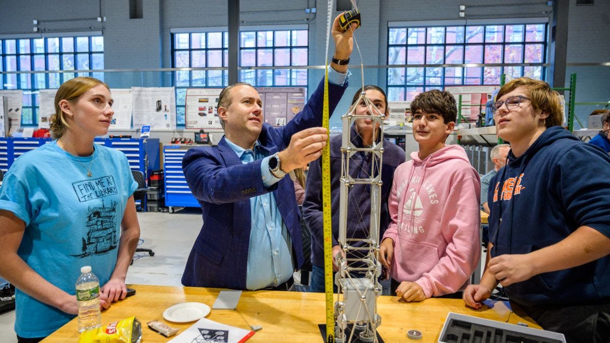 Photo of a man holding up a measuring tape to a tower while four students surround him looking up