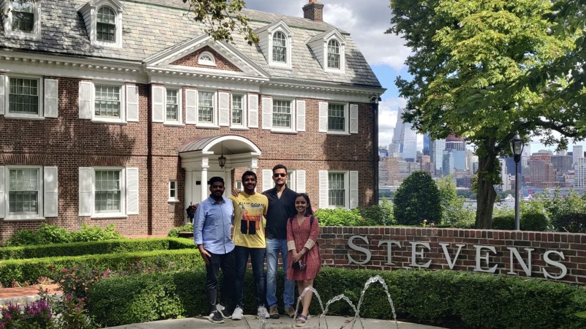 Rhythm Goyal stands with her family in front of the fountain on the Stevens campus with the New York City skyline visible in the background.