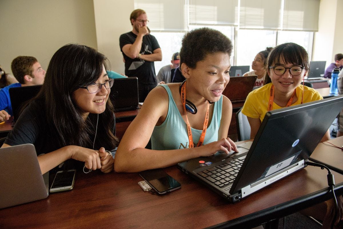 Three female students in front of a laptop in a pre-college classroom
