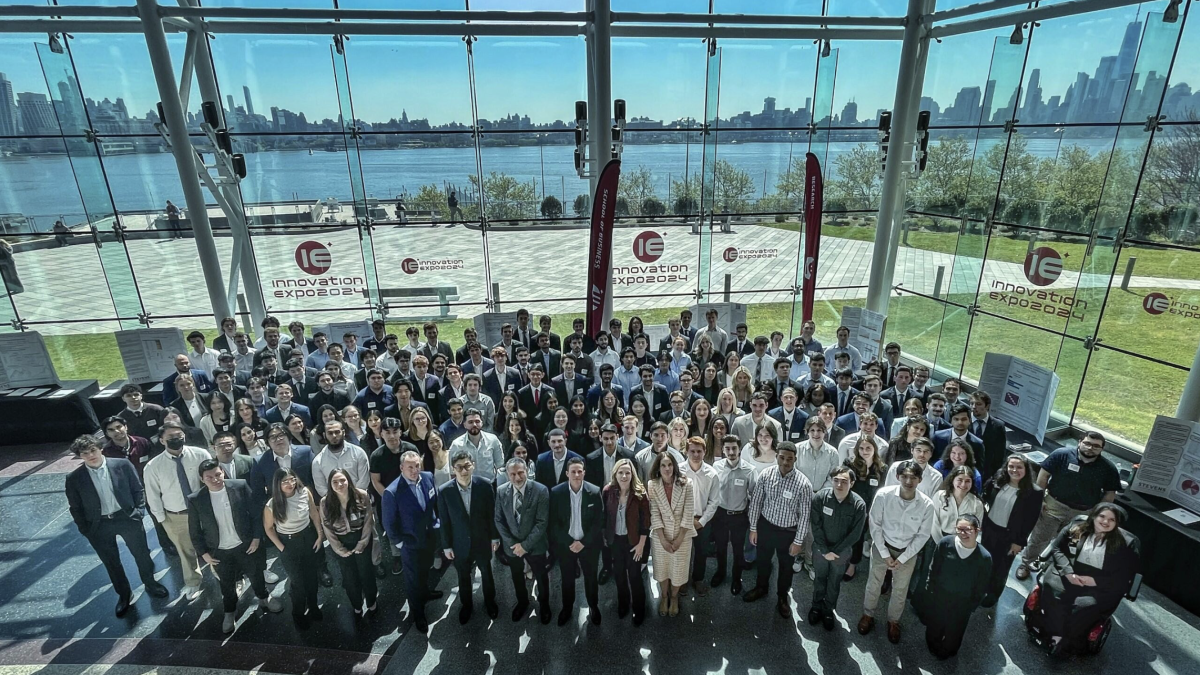 A group shot of the participants in front of the glass atrium walls with the Hudson River and New York City skyline in the background.
