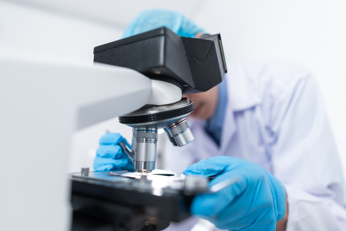 Photo of a man in white lab coat looking through a microscope