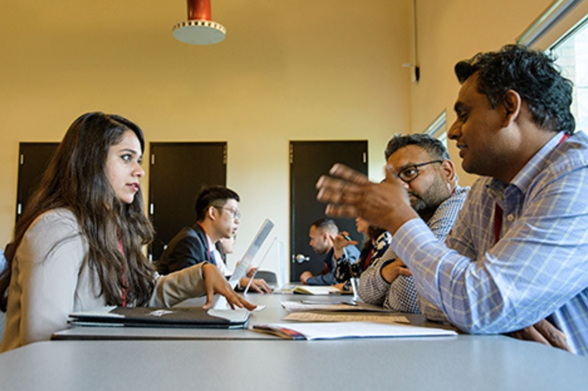 A female student listens to a make recruiter at a conference table on campus.