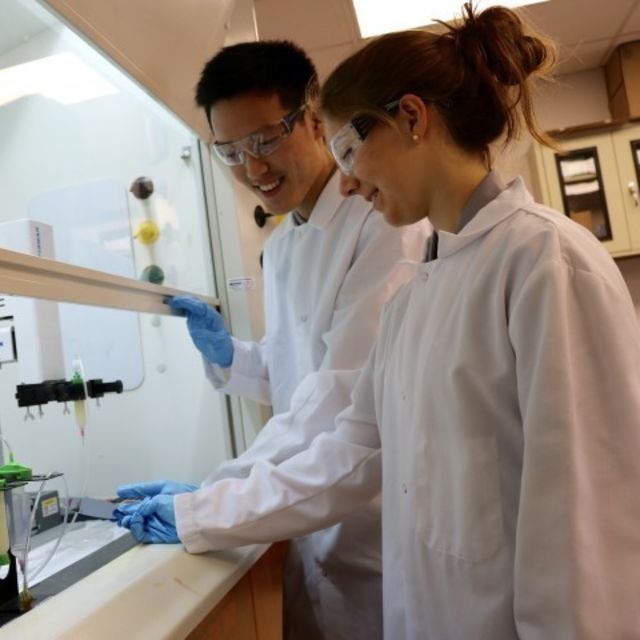 A photo of two students wearing lab gear looking at test tubes