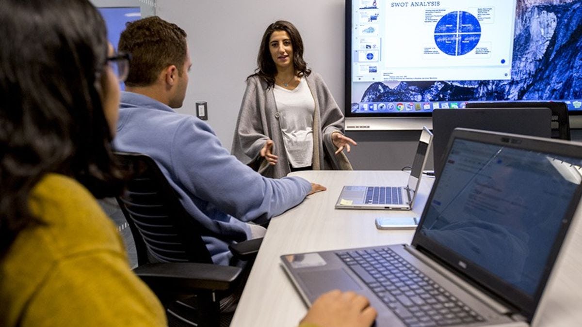 One male and two female students collaborate in a high-tech conference room at Stevens.