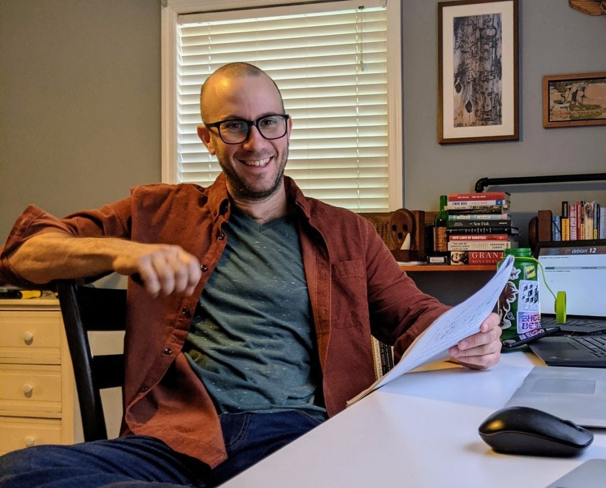 Michael Greenberg sits at a desk at home, smiling at the camera