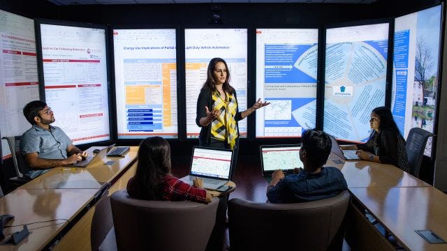 Instructor teaches small class in front of immersion wall of data