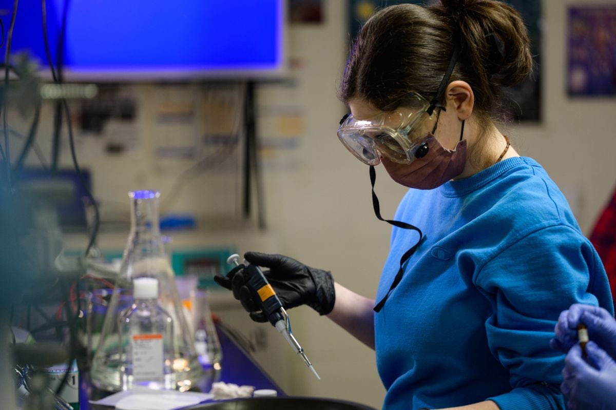 A student wearing safety goggles works with chemical equipment in a lab.