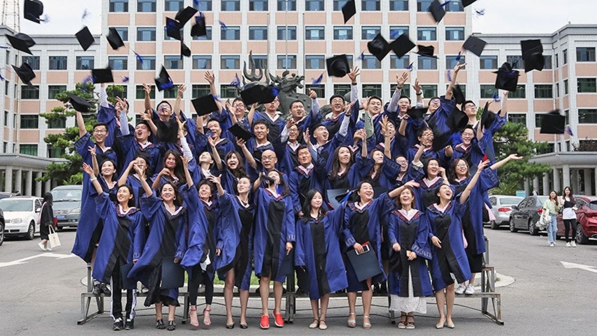 A group of students at CUFE in graduation regalia throwing their caps in the air. 