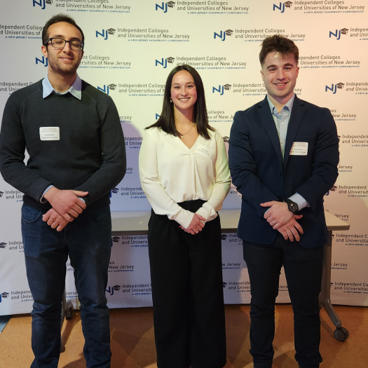 Amir Ibrahim ’25, Jenna Booth ’23 and Gabriel Sorci ’25 pose in front of a branded backdrop at ICUNJ 2023