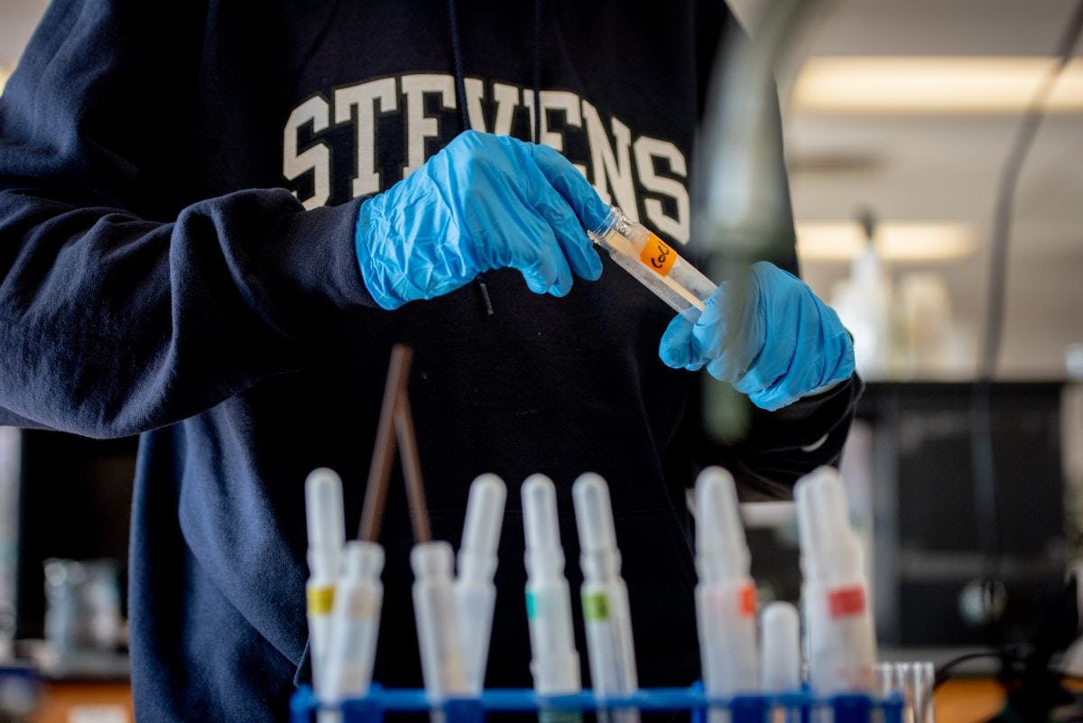 Student in a Stevens sweatshirt handling test tubes in a lab.