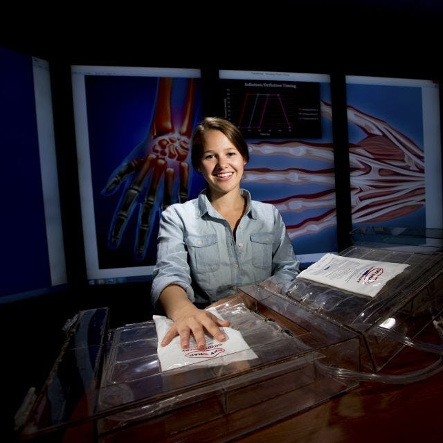 A photo of a female student sitting at a table with images of the physiology of a hand in the background