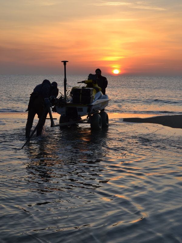 Members of the Department of Civil, Environmental and Ocean Engineering bring a device onto the shore with the sun going down.