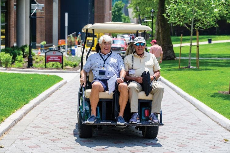 Alumni riding down Whittpenn walk on the back of a golf cart.