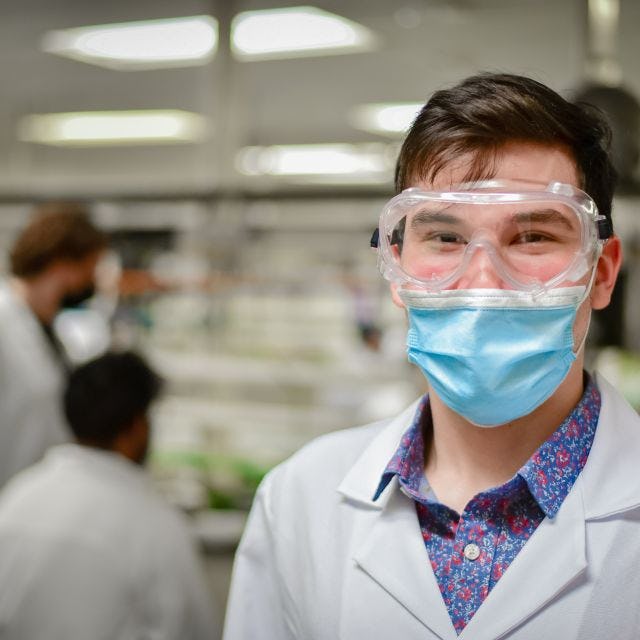 lab student with goggles and a mask on looking into camera