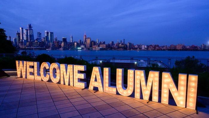 Welcome Alumni sign on Babbio Patio with the New York City skyline in the background  
