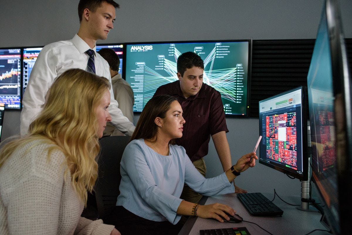 alt="Student points to interesting information on computer monitor while other students look on, intrigued"