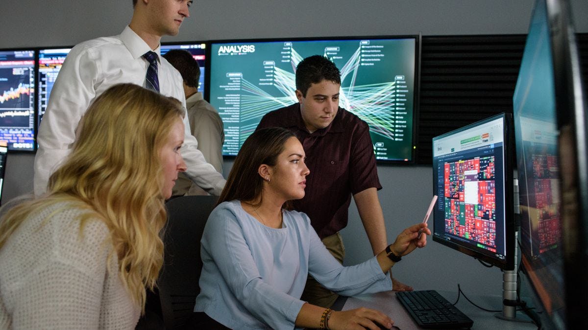 Student points to interesting information on computer monitor while other students look on, intrigued