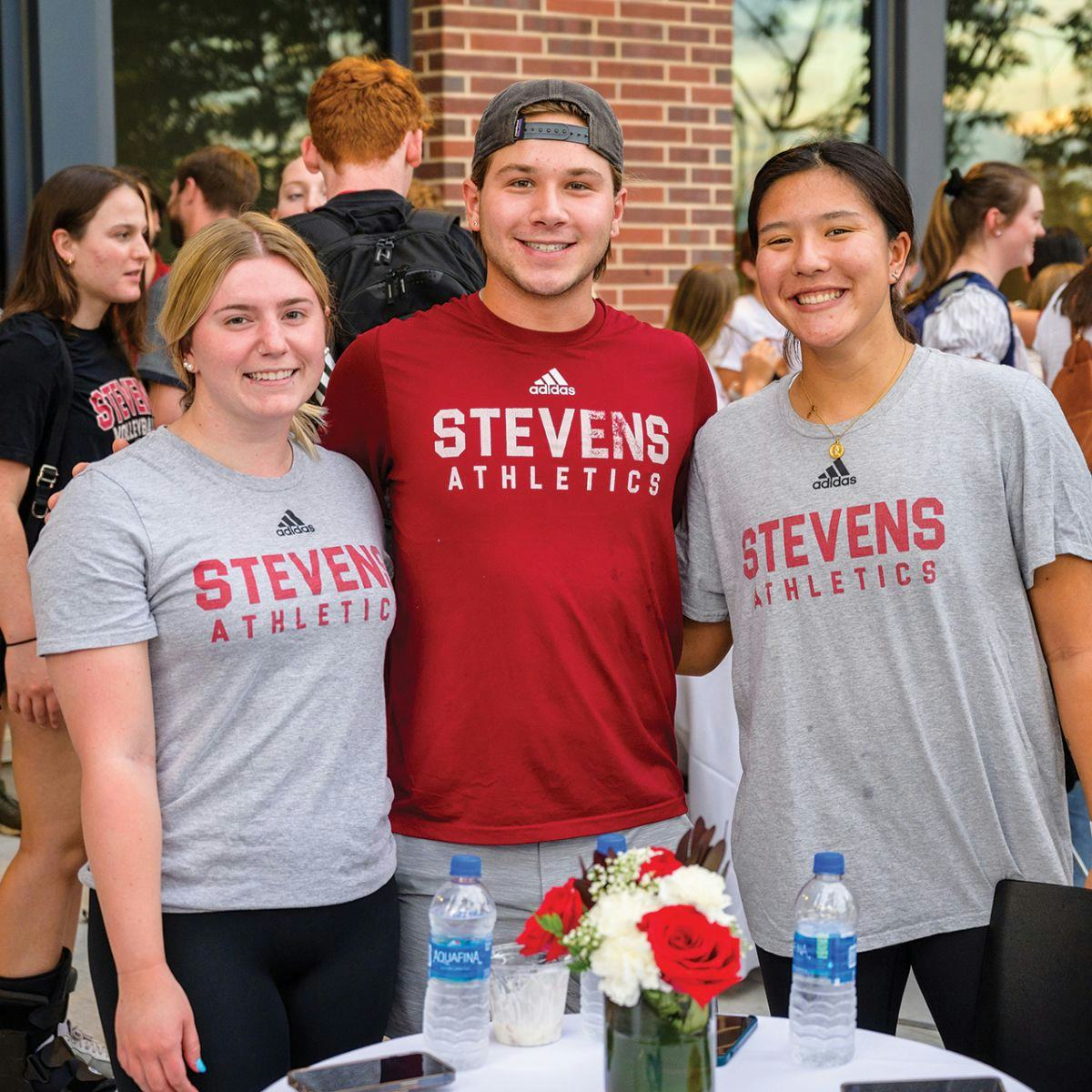 Three student athletes smile for camera at a celebration on campus.