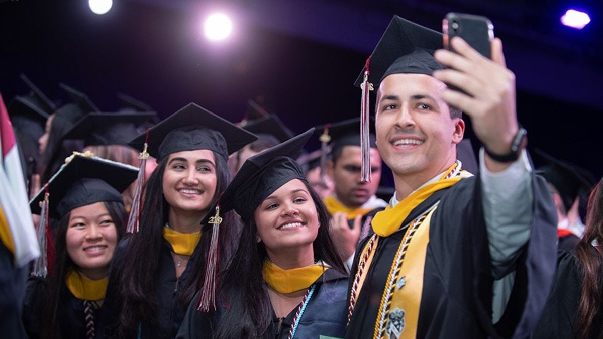 Three female students pose for a selfie taken by a fourth student. All are in their graduation regalia.