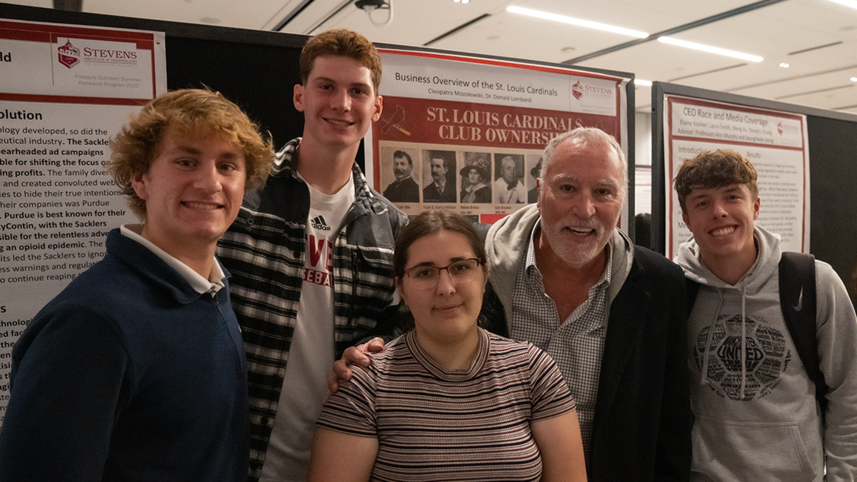 Professor Don Lombardi stands with a group of students at the 2023 Pinnacle Scholars poster exhibition.