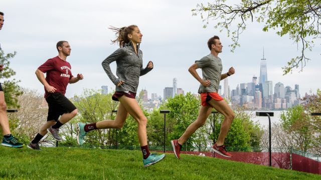 Students jog across campus with New York city in background