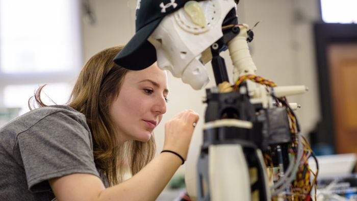 Student working on a white robot wearing a black Stevens hat with wires showing in its back