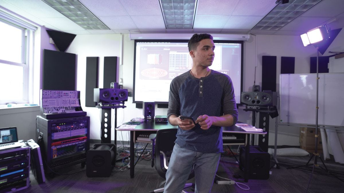 Student in audio lab, with speakers and equipment.