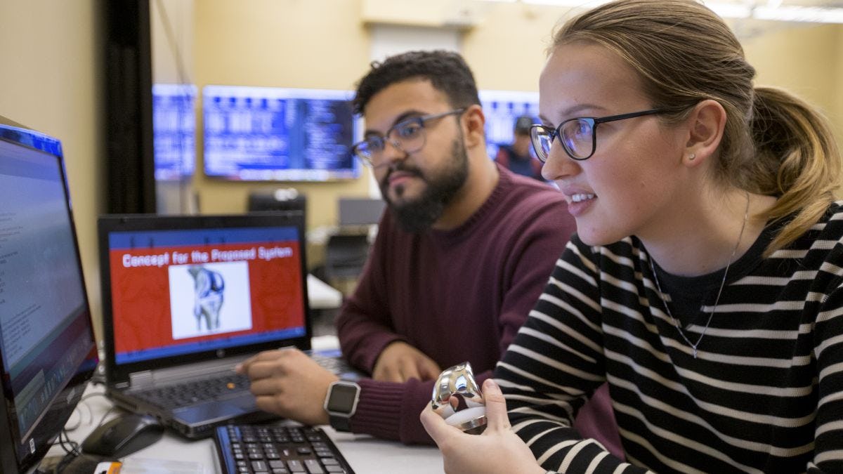 Two software engineering students look at a shared monitor during class.