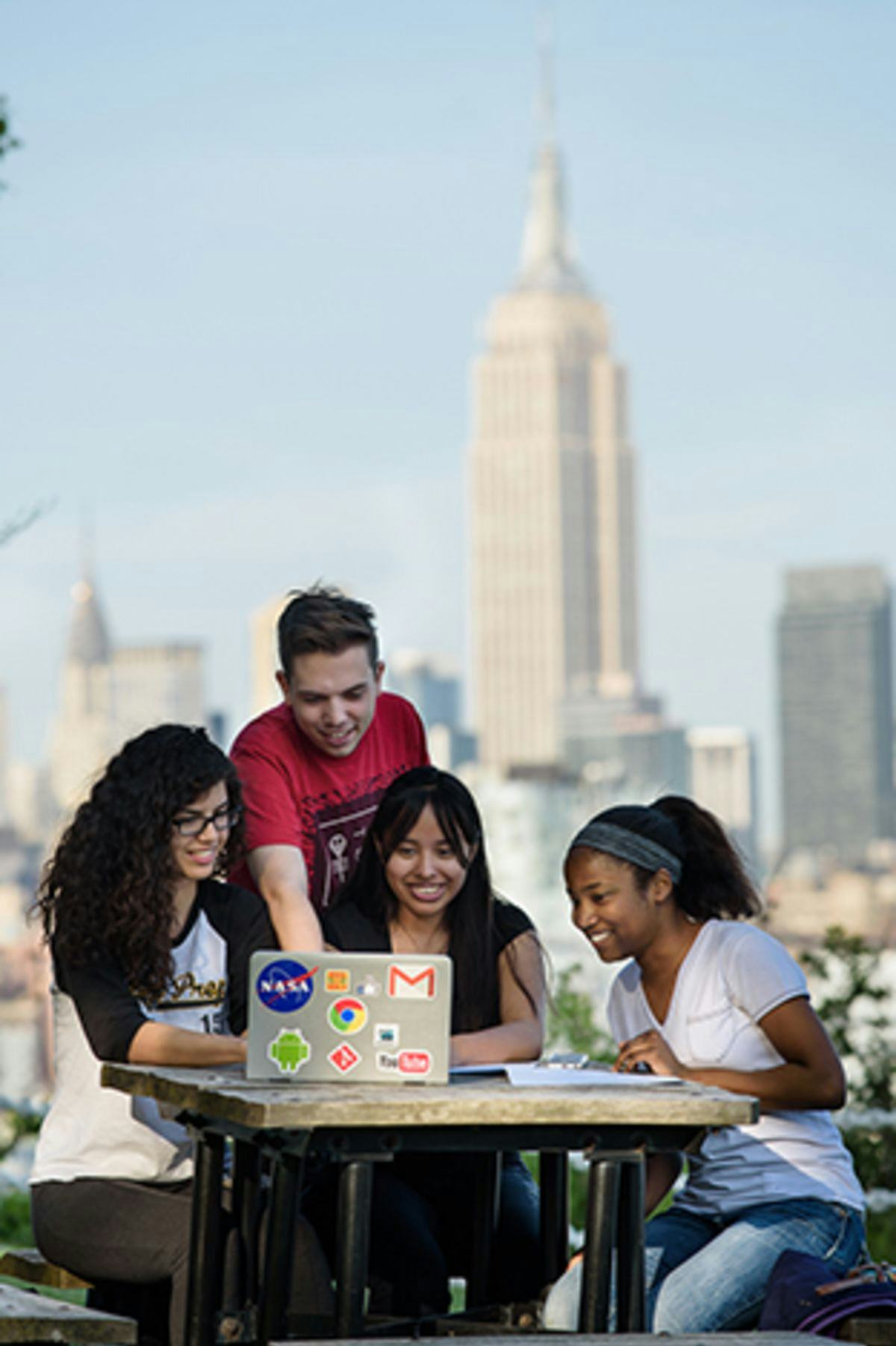 A group of students look at their computers with the Empire State Building in the background.