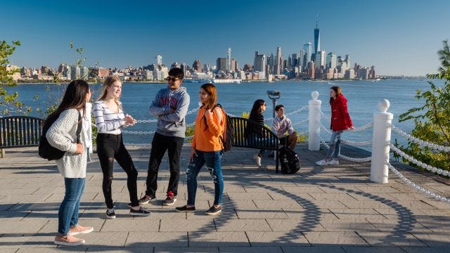 Students socialize at Castle Point with New York skyline in background.