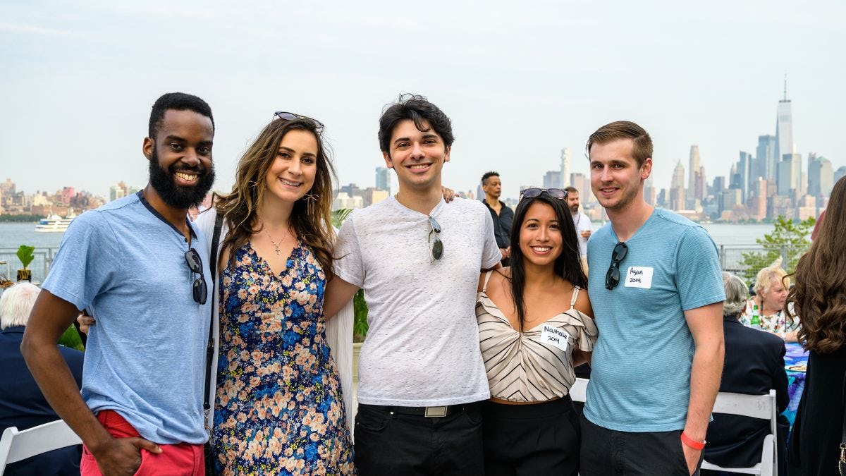 Five Stevens alumni pose for a photo outdoors in front of the New York skyline.