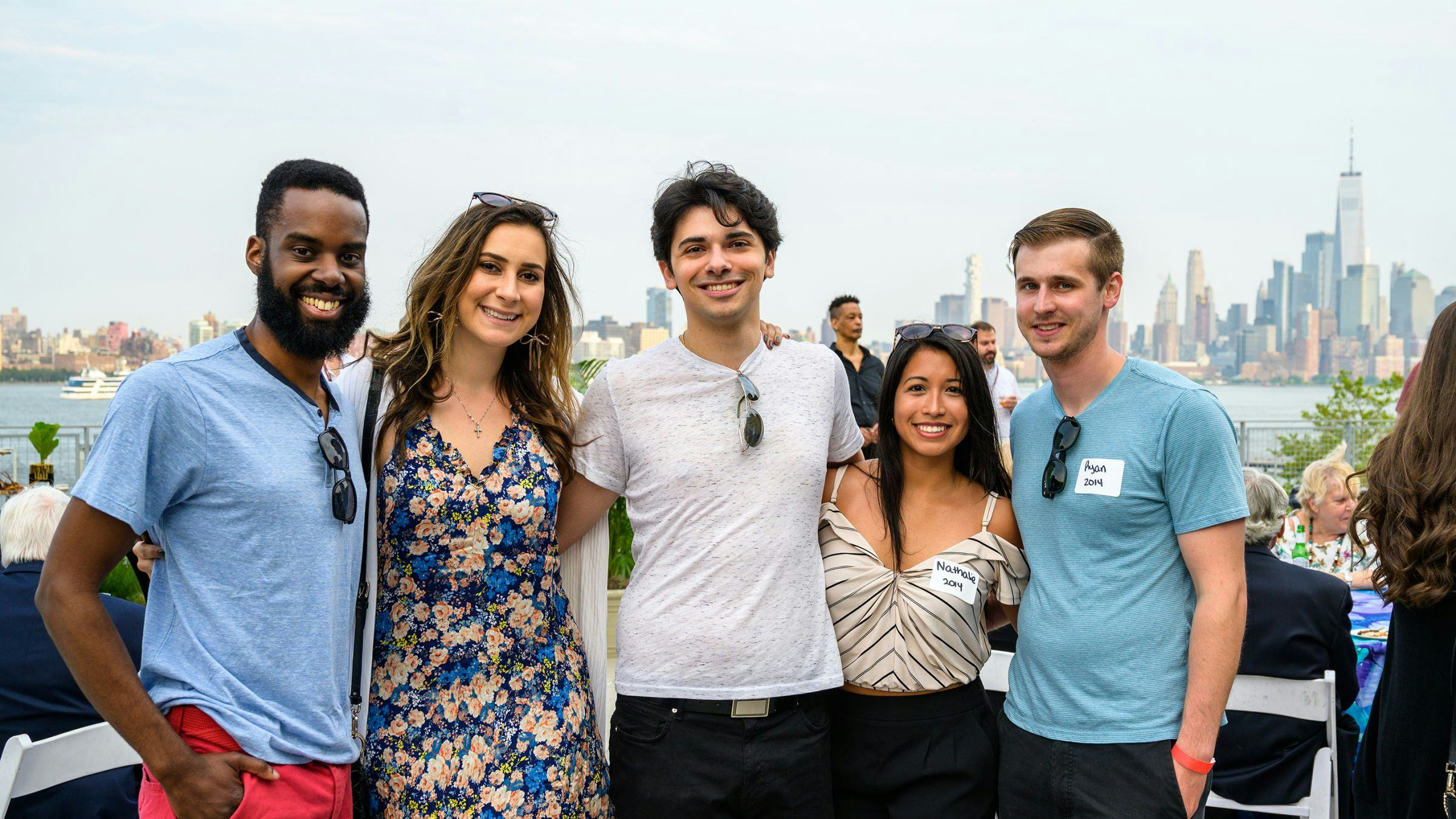 Five Stevens alumni pose for a photo outdoors in front of the New York skyline.