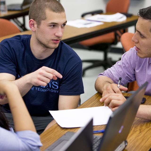 Three graduate systems engineering students work together at a table during class.