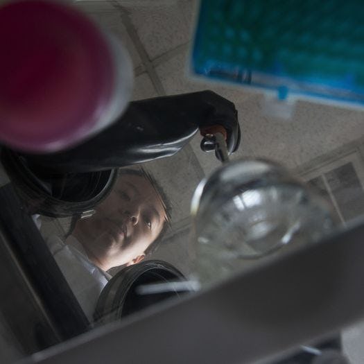 Photo of female student experimenting in lab, from the angle of beneath a glass table of her looking down