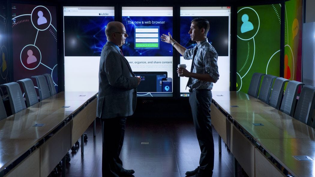 A faculty and a student talking in the immersion lab surrounded by screens
