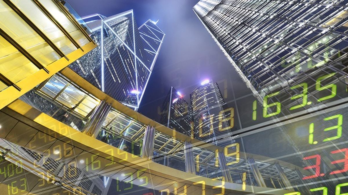 The Hong Kong skyline at night with a stock ticker projected over it. 