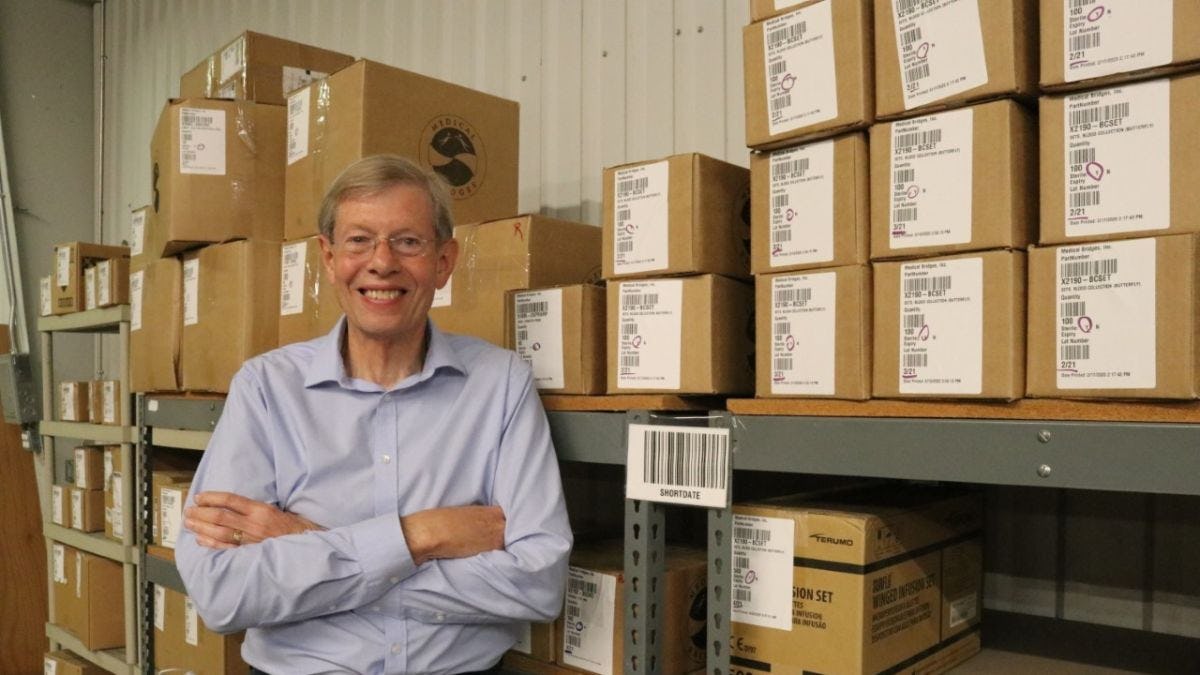 Walter Ulrich '68 posing with stacks of boxes at the nonprofit's warehouse