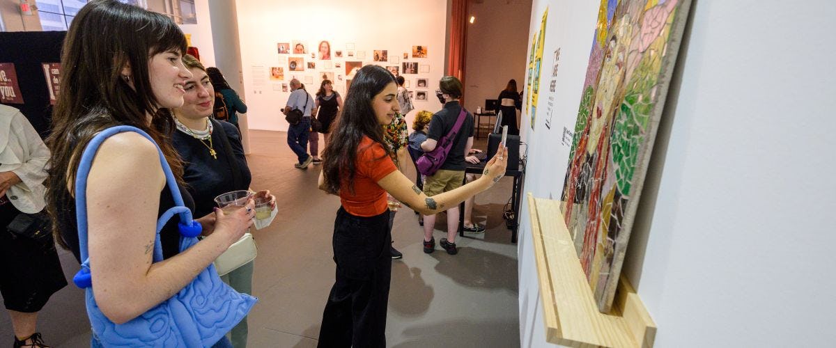 Three students look at a mosaic at the visual arts and technology senior exhibition