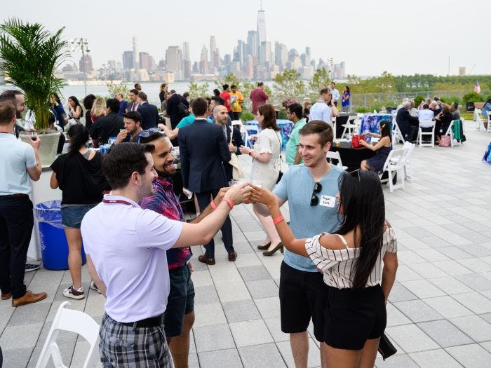 Four Stevens alumni toast their glasses on the Babbio plaza with the New York Skyline in the distance.