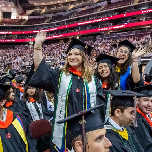 Graduates standing and waving to the crowd at the 2023 Commencement ceremony