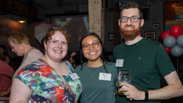 Three young alumni hold drinks and smile at event