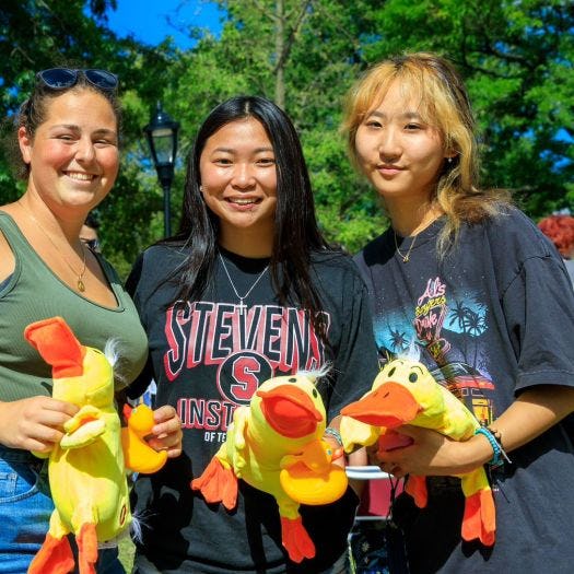 Three students smile and hold stuffed animal ducks