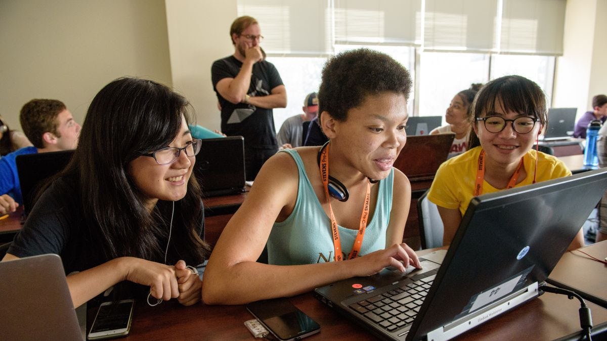 Three female students in front of a laptop in a pre-college classroom