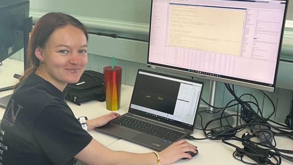 Photo of Samantha Gajda smiling at the camera while working on a computer