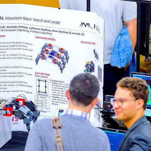 Student explains a crab-like robot to a visitor at the 2023 Stevens Innovation Expo