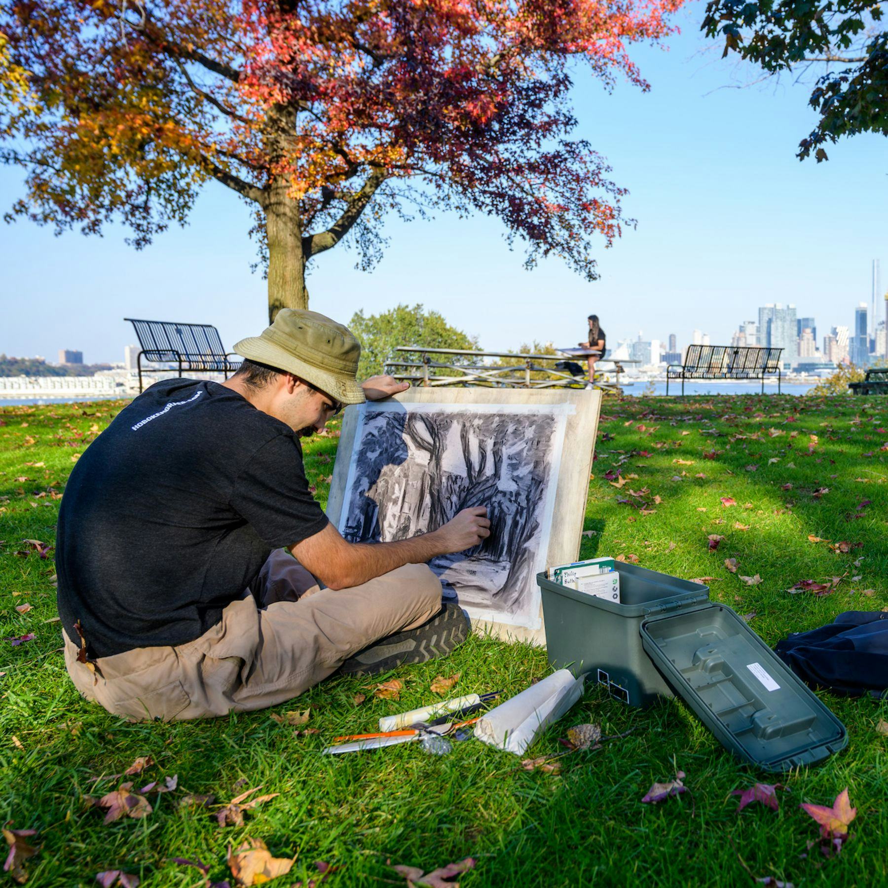 Student drawing while sitting on grass with NYC in the background