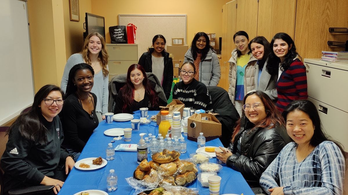 The Stevens team -- staff and students -- eat bagels around a table to celebrate their success at Introduce a Girl to Engineering! Day