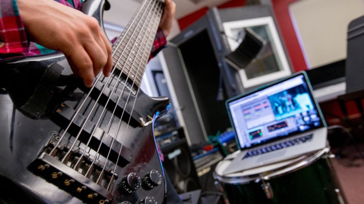 Student plays guitar and records sound onto laptop